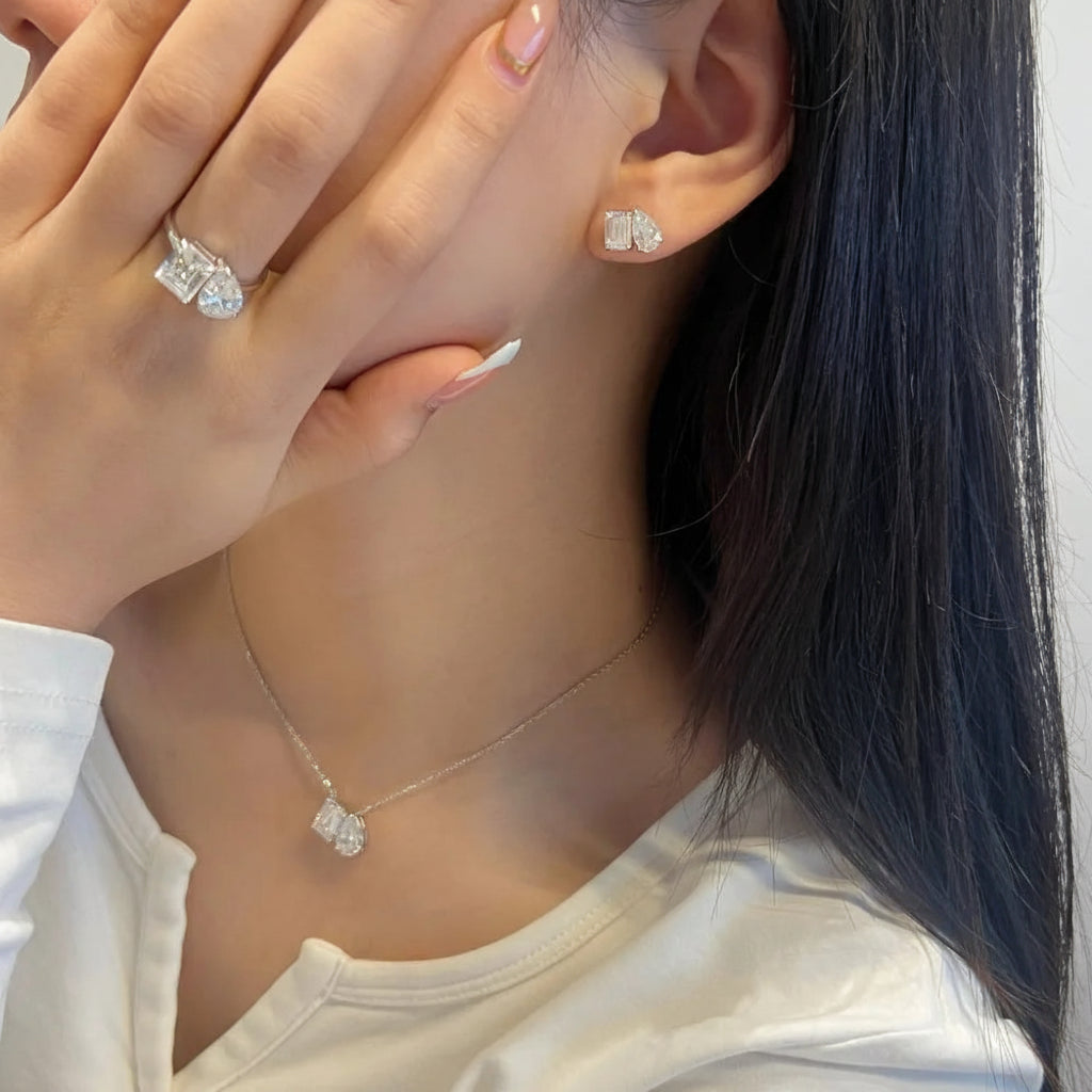 Close-up of a person wearing diamond earrings and a necklace, with one hand covering their face.