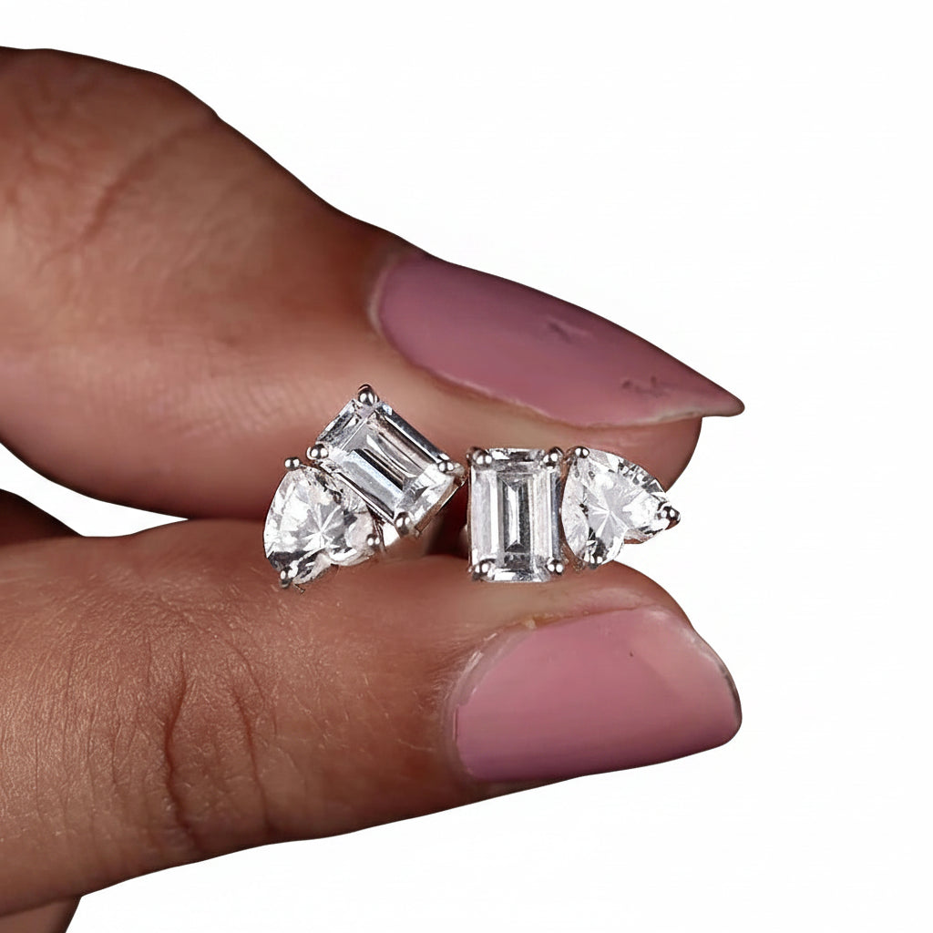Pair of diamond earrings held between fingers with a white background