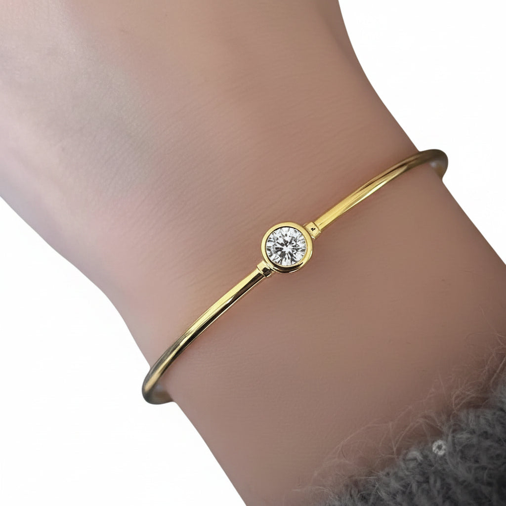 Gold bracelet with a diamond on a wrist against a neutral background