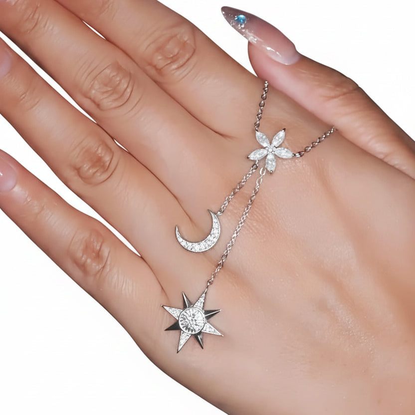 Silver necklace with star, moon, and sun pendants on a hand against a white background