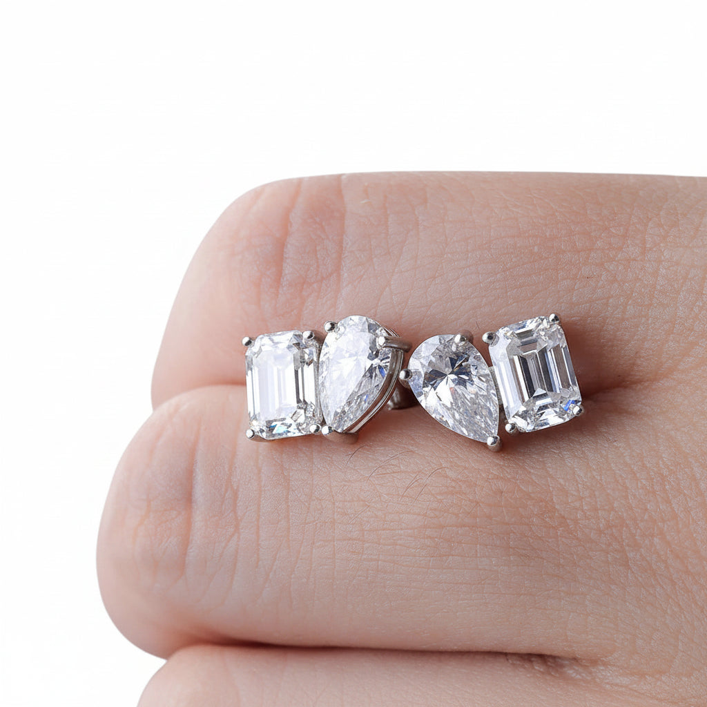 Diamond rings with pear-shaped and emerald-cut diamond between fingers.