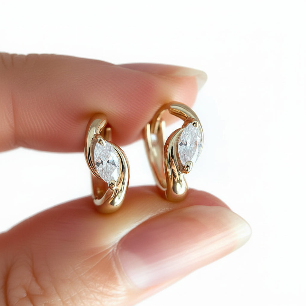 Gold earrings with marquise-shaped gemstones held between fingers against a blurred white background
