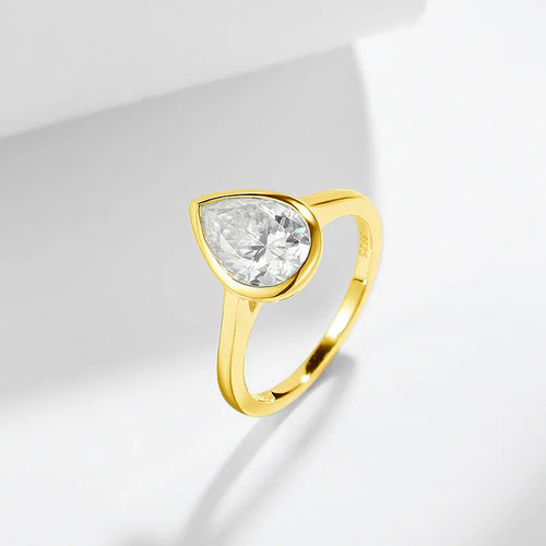 Gold ring with a clear pear moissanite gemstone on a light gray background