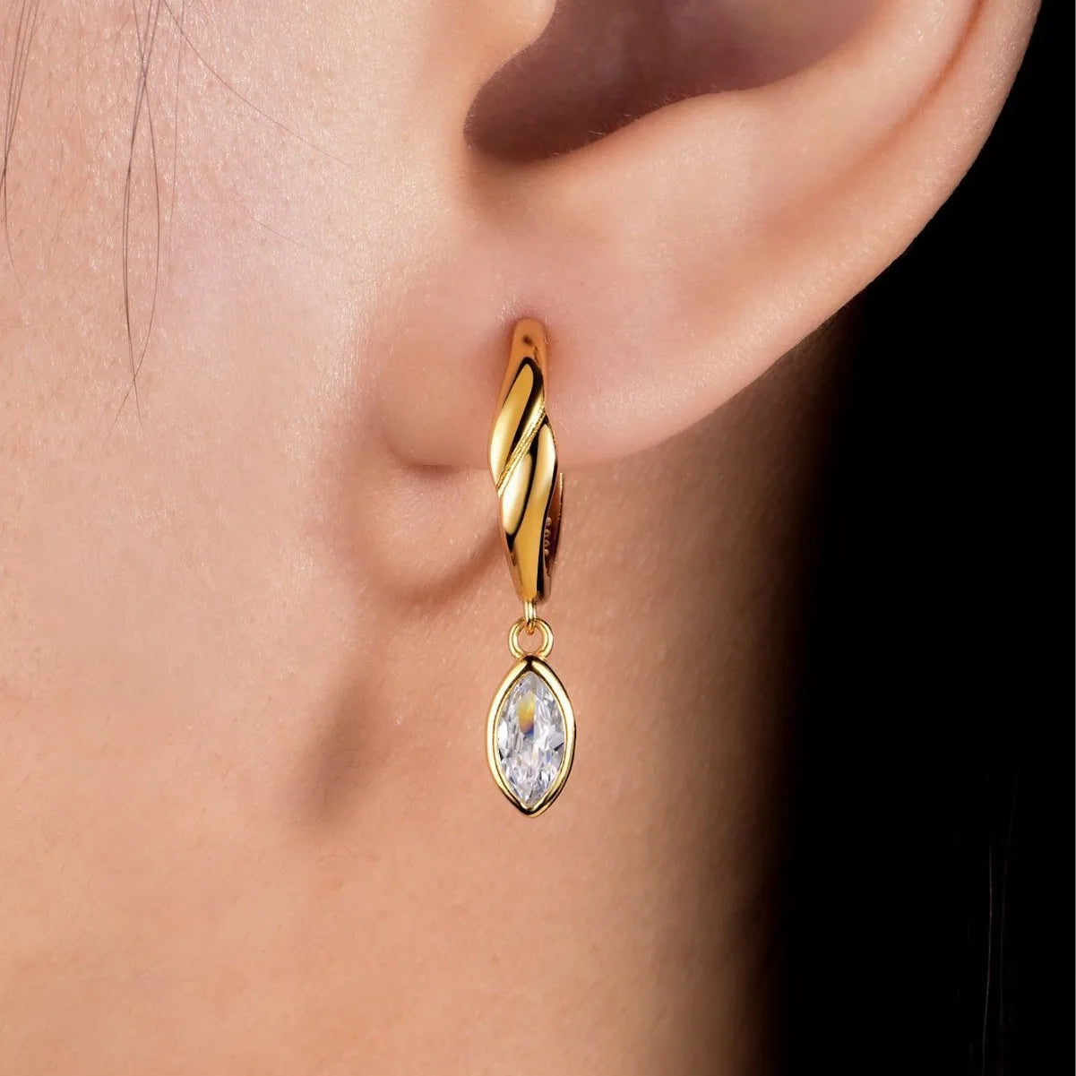 Gold earring with a moissanite gemstone worn on an ear