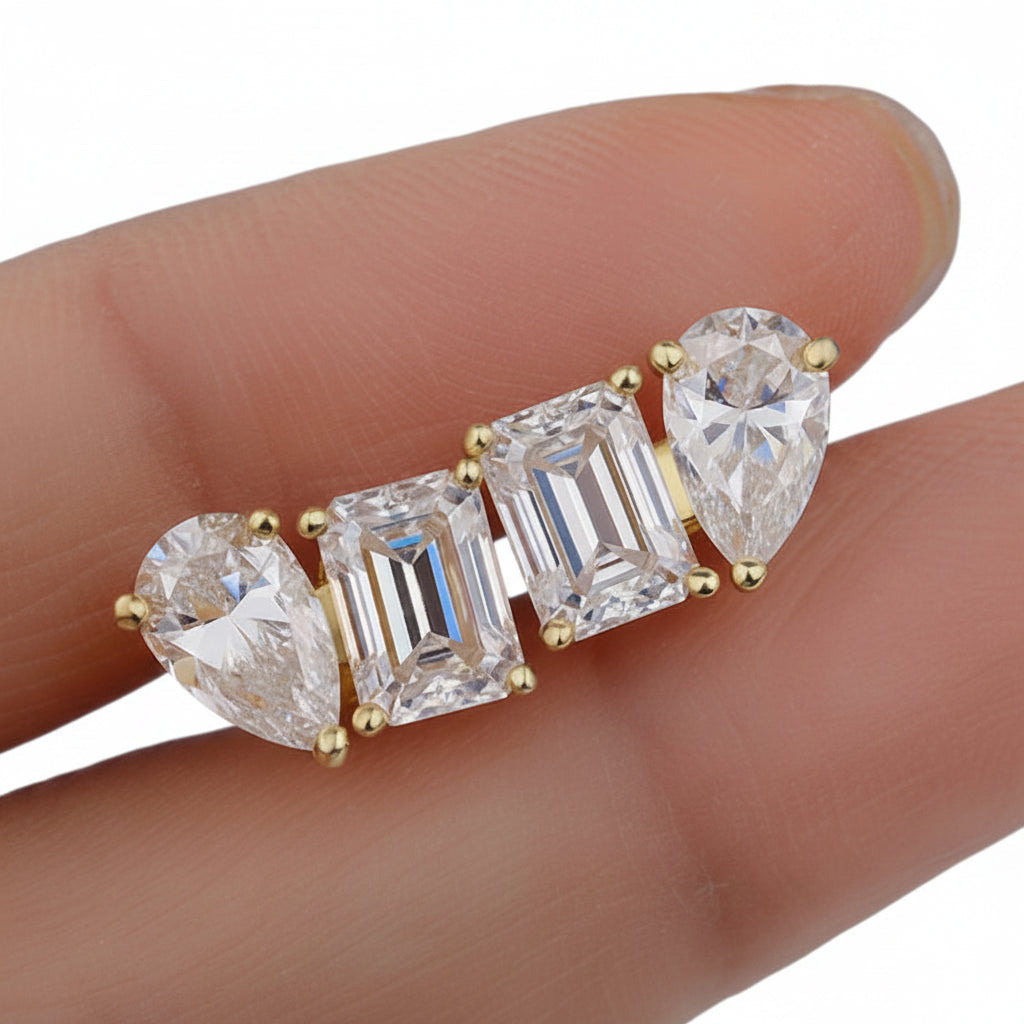 Gold ring with pear-shaped and emerald-cut moissanite gemstones on a hand.