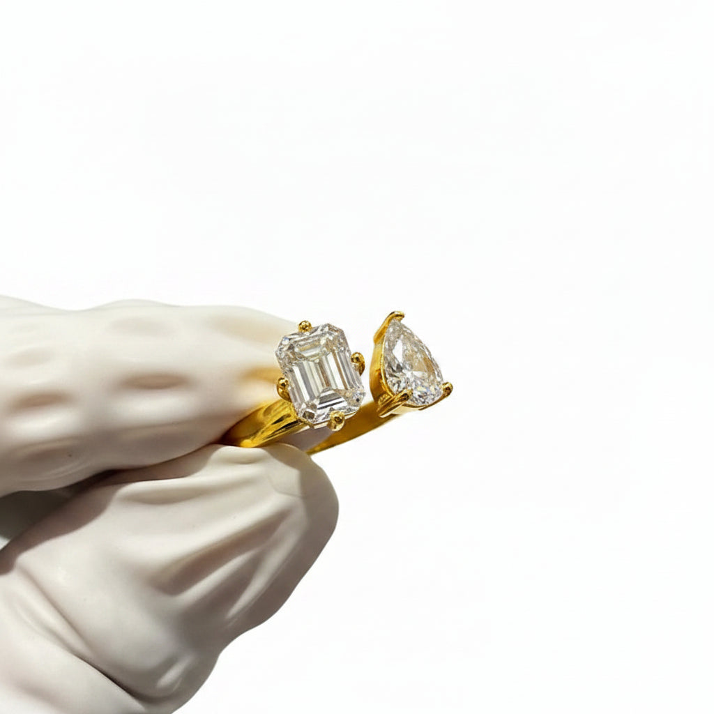 Gold ring with moissanite stones held by a gloved hand against a white background