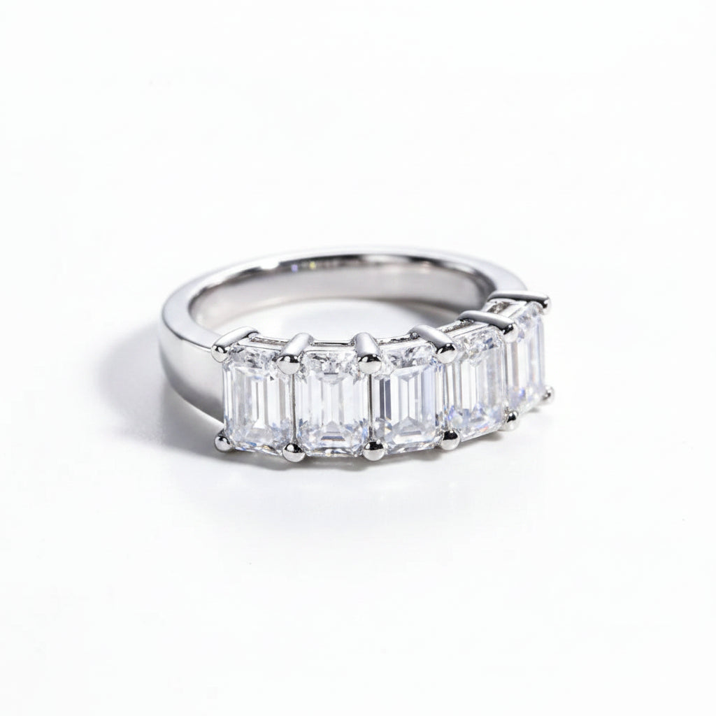 Silver ring with emerald-cut gemstones on a white surface