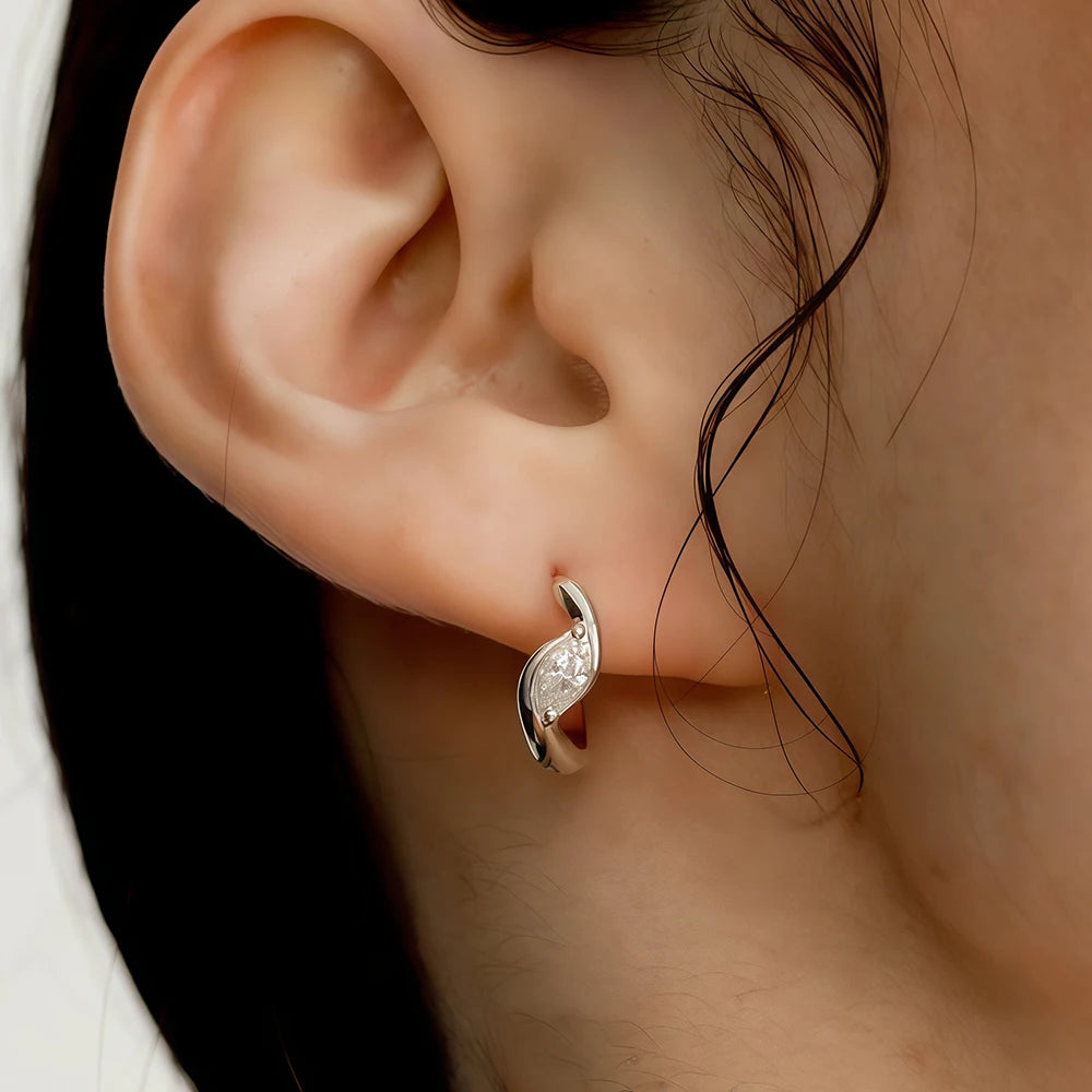 Close-up of an ear wearing a silver earring with a clear gemstone.
