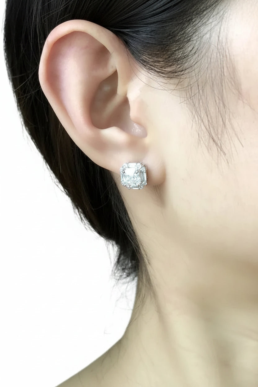 Close-up of a person wearing a silver stud earring with a clear gemstone against a neutral background