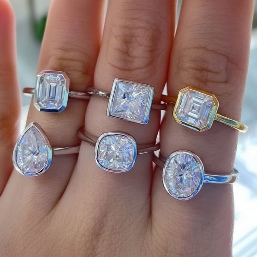 Hand wearing multiple moissanite diamond rings with various cuts and settings.