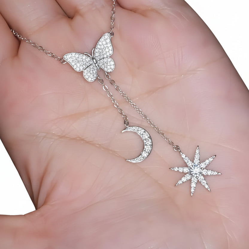 Necklace with star, moon, and sun pendants held in a hand.