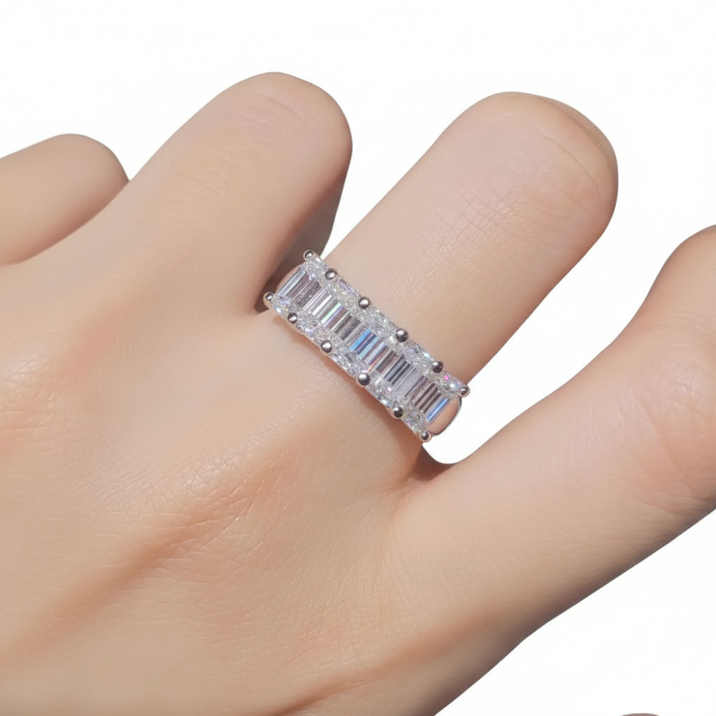 Silver ring with emerald-cut gemstones on a finger against a neutral background