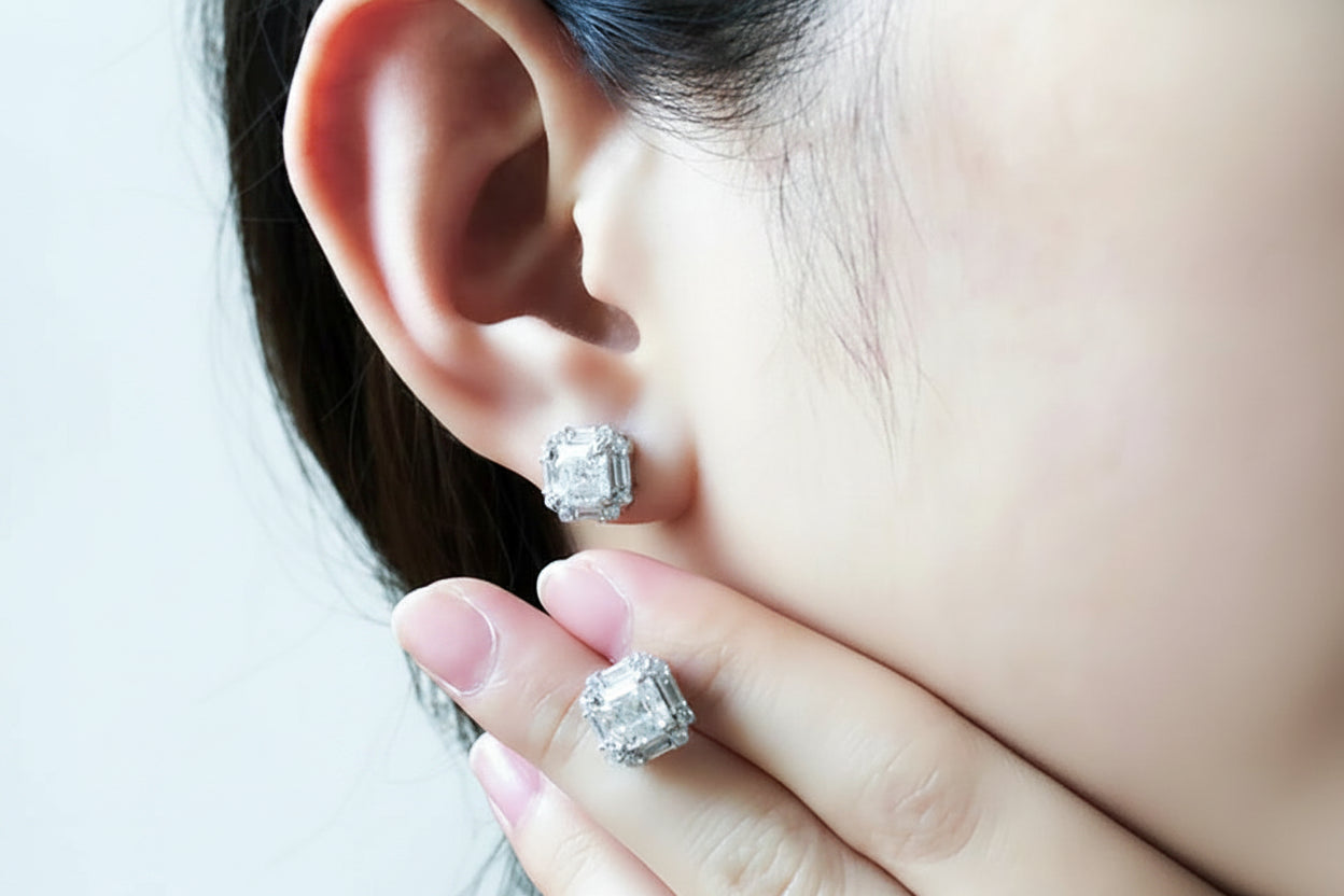 Close-up of a person wearing diamond stud earrings with a neutral background