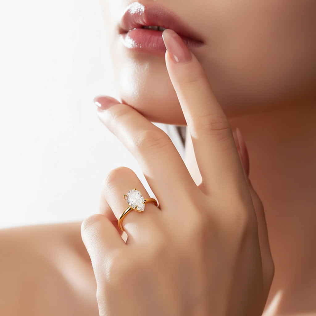 Close-up of a hand with a gold ring featuring a pear-shaped diamond, touching the cheek.