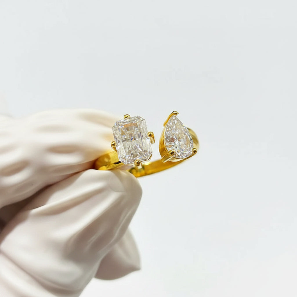 Gold ring with pear-shaped moissanites held by a white hand against a white background