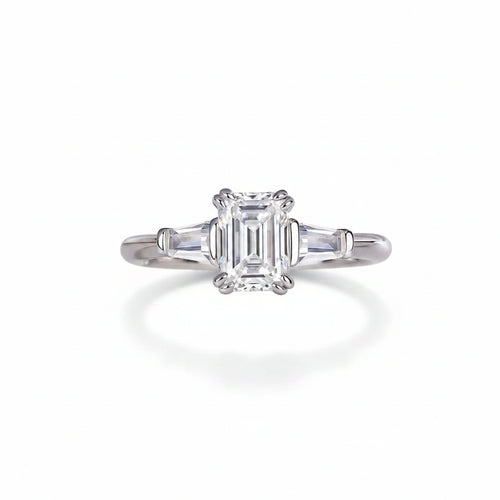 Moissanite ring with emerald-cut center stone on white surface