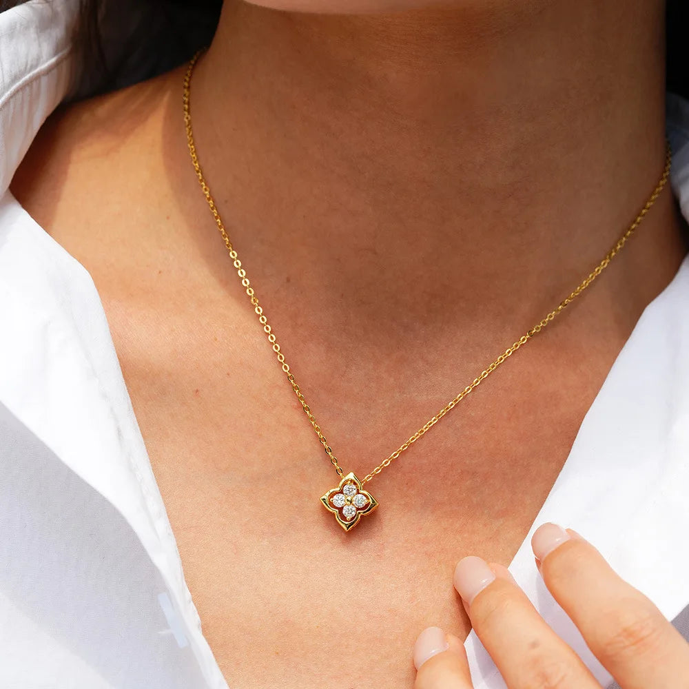 Gold necklace with a clover-shaped pendant worn by a person in a white shirt.