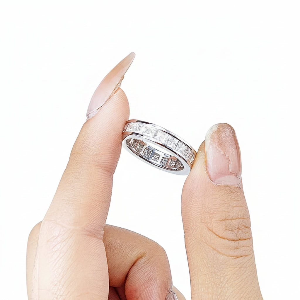 Hand holding a silver ring with gemstones against a white background