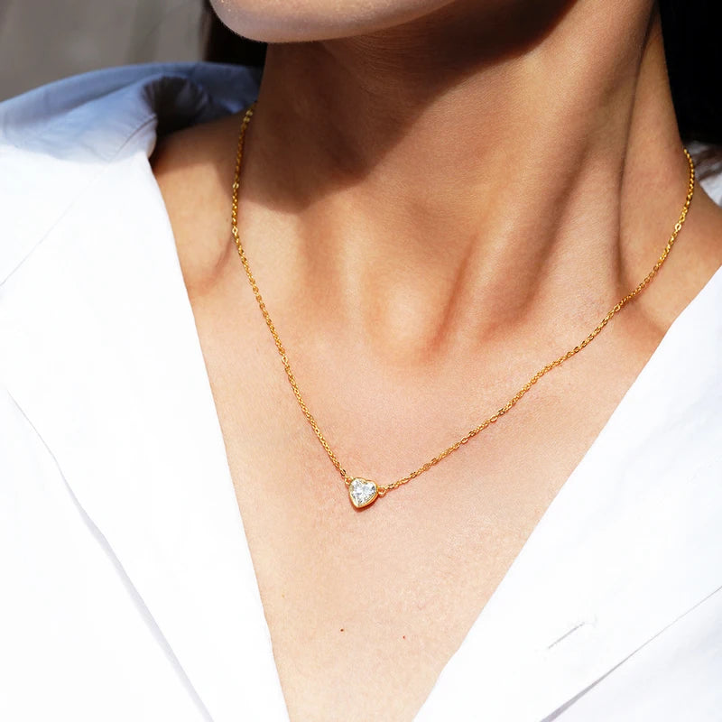 Gold necklace with a heart-shaped pendant worn by a person against a neutral background
