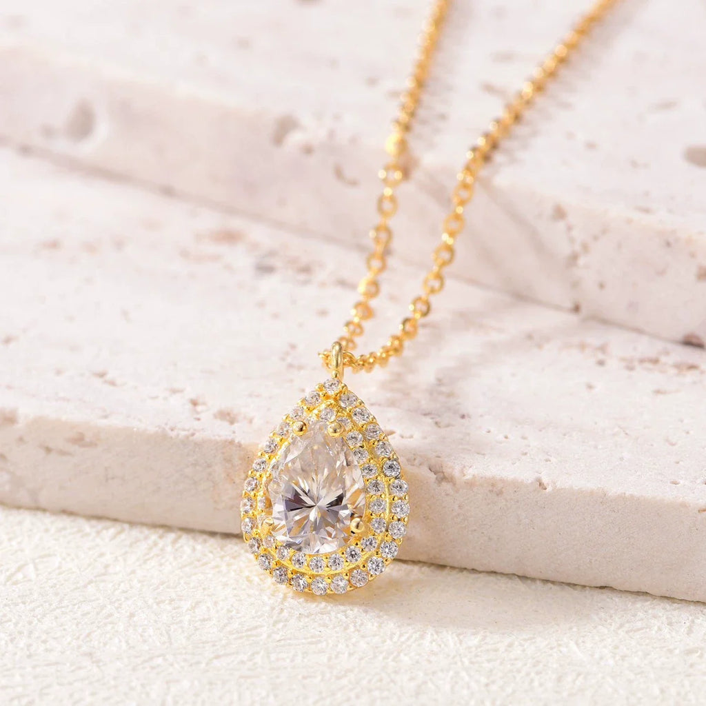 Gold necklace with a teardrop-shaped moissanite pendant on a light background