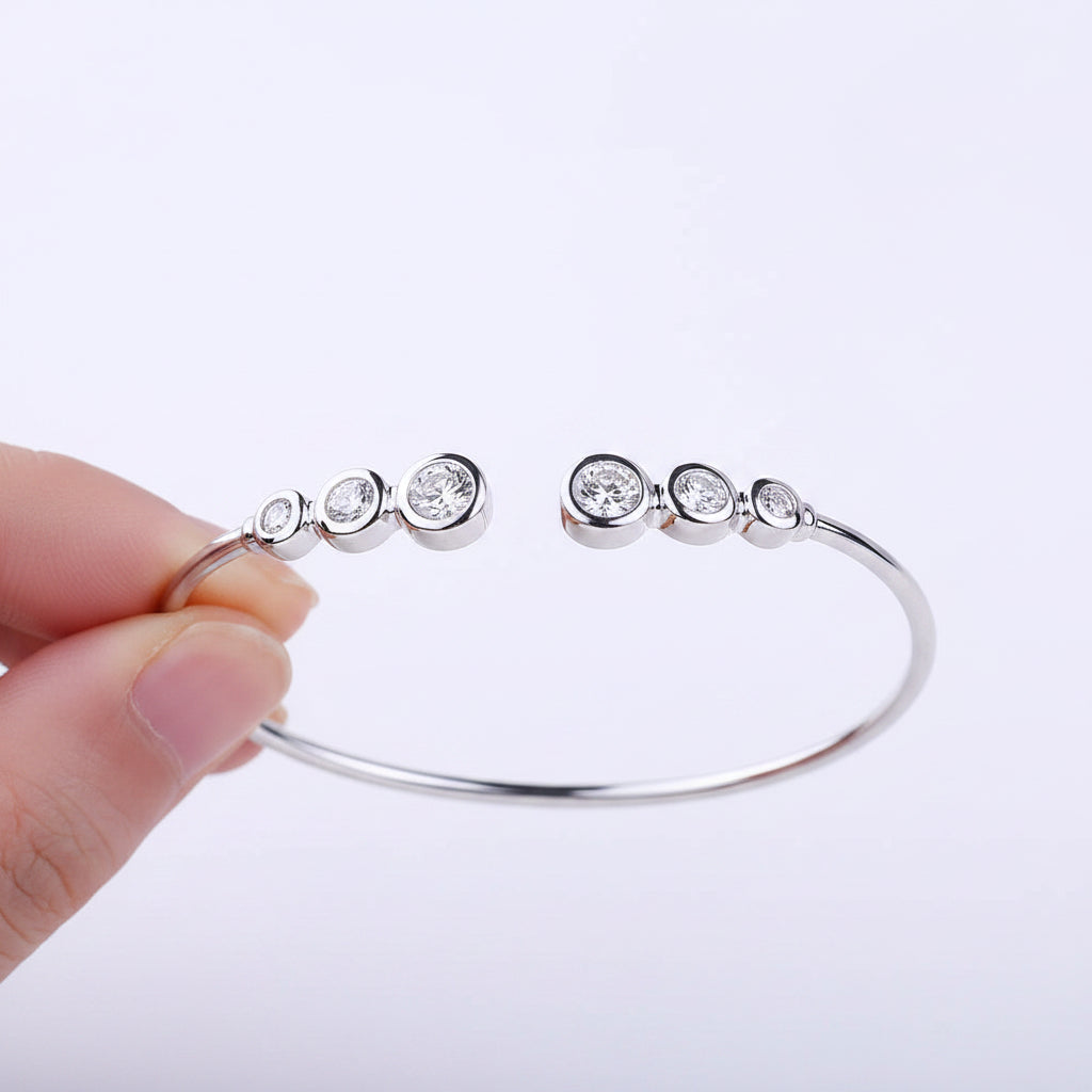Silver bracelet with six moissanite stones held by a hand against a neutral background