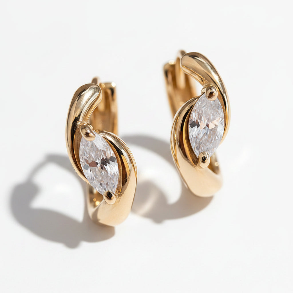 Gold earrings with clear gemstones on a reflective white surface
