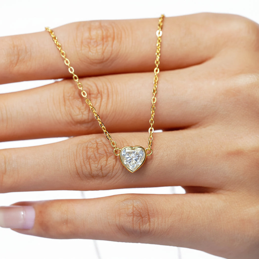 Gold necklace with a heart-shaped diamond pendant on a hand against a white background