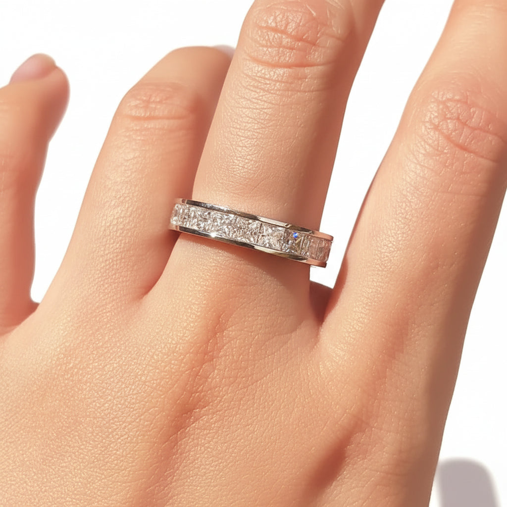 Silver ring with moissanites on a person's finger.