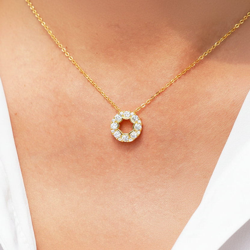 Gold necklace with a circular pendant on a person wearing a white shirt.