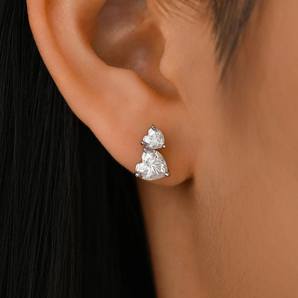 Close-up of a person wearing a pair of heart-shaped moissanite diamond earrings.