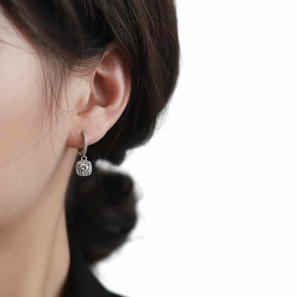 Close-up of an ear wearing a silver earring with a moissanite gemstone on a neutral background