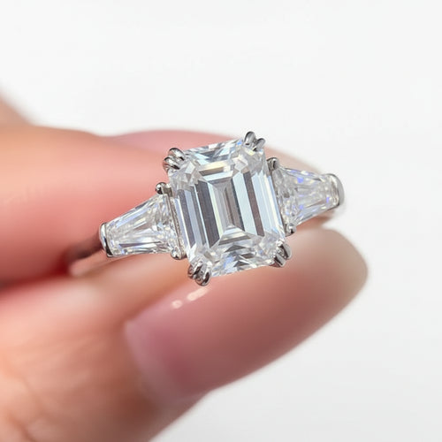 Emerald moissanite ring held between fingers.