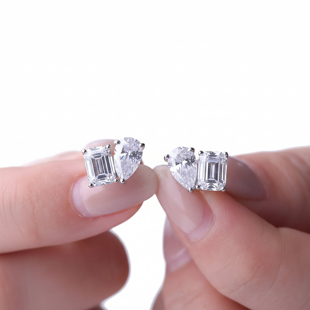 Moissanite diamond earrings held between fingers against a white background