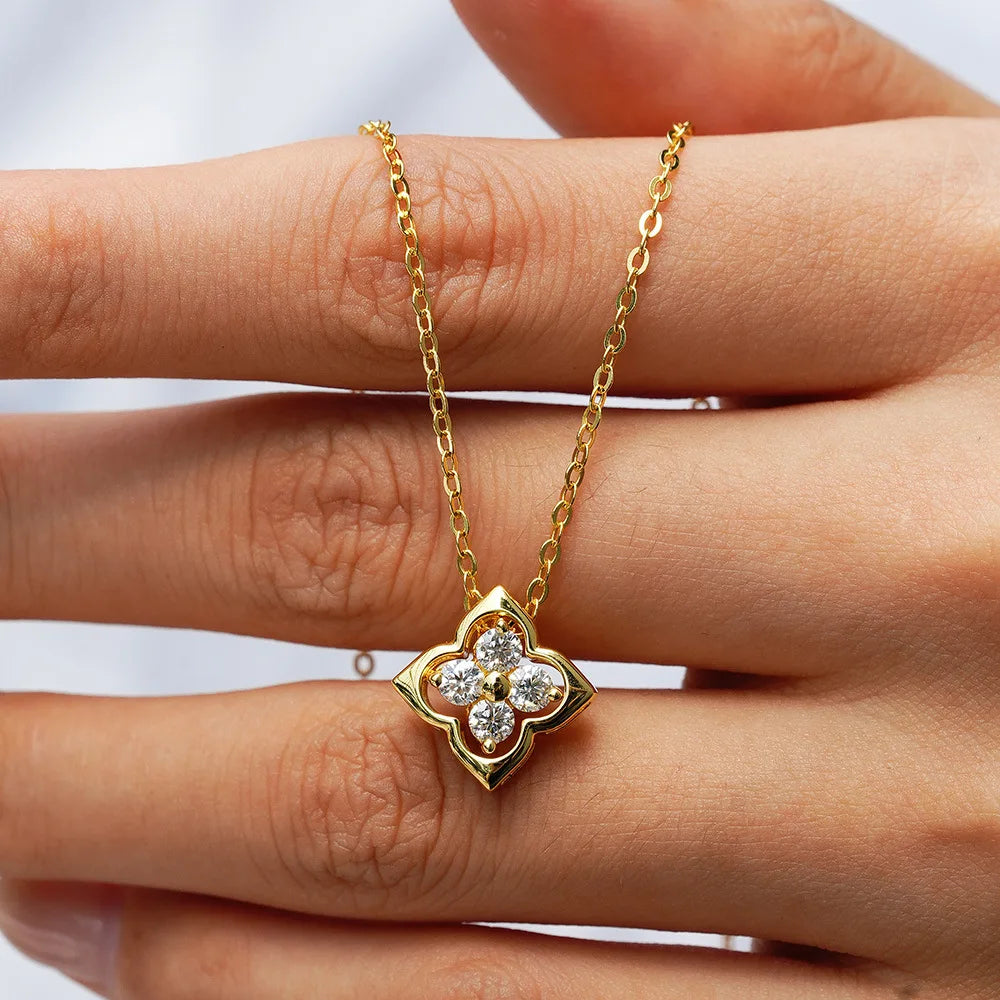 Gold necklace with a clover-shaped pendant on a hand against a white background